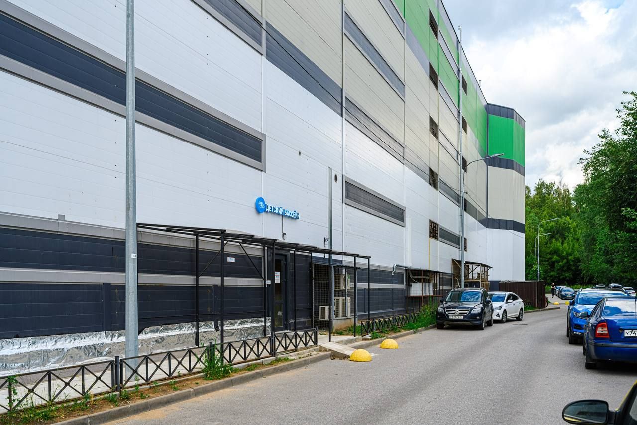 Street view of a modern industrial building with a sign, parked cars, and a cloudy sky.