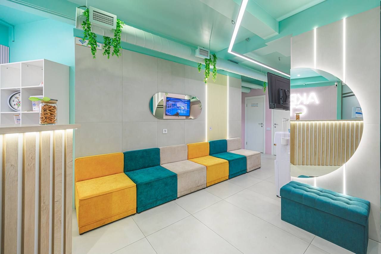 Modern waiting area with colorful seating, wall-mounted TV, decorative plants, and soft lighting. Bright and inviting atmosphere.
