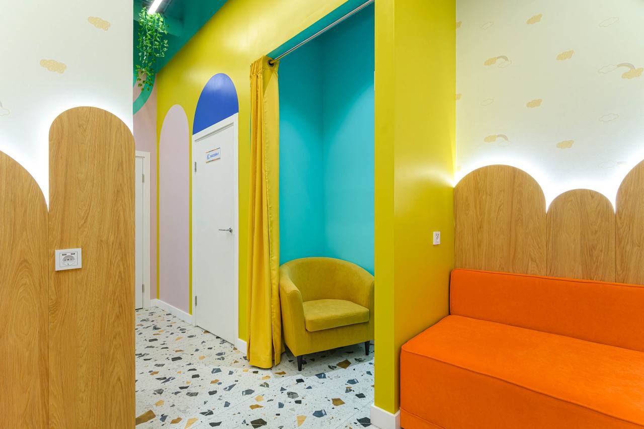 Bright, colorful room with yellow walls, orange seating, terrazzo floor, and a cozy yellow chair in a turquoise alcove.