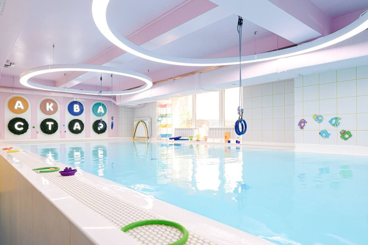 Indoor pool with colorful alphabet decorations on the wall, floating toys, and circular lights on the ceiling.