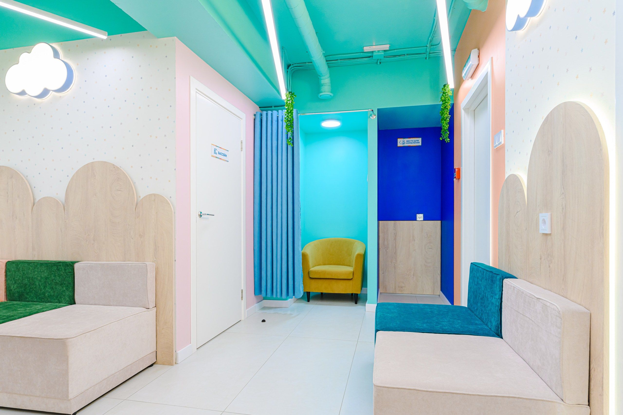 Colorful waiting room with pastel walls, cloud-shaped decor, green and beige seating, a yellow chair, and a blue privacy curtain.