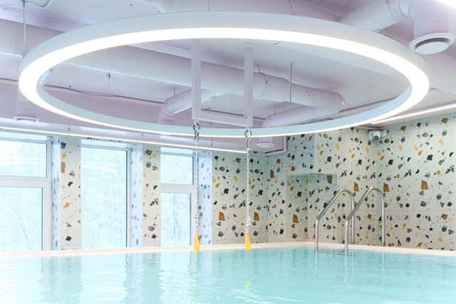 Indoor pool with terrazzo walls, large circular ceiling light, and two hanging yellow swings. Snowy windows in the background.